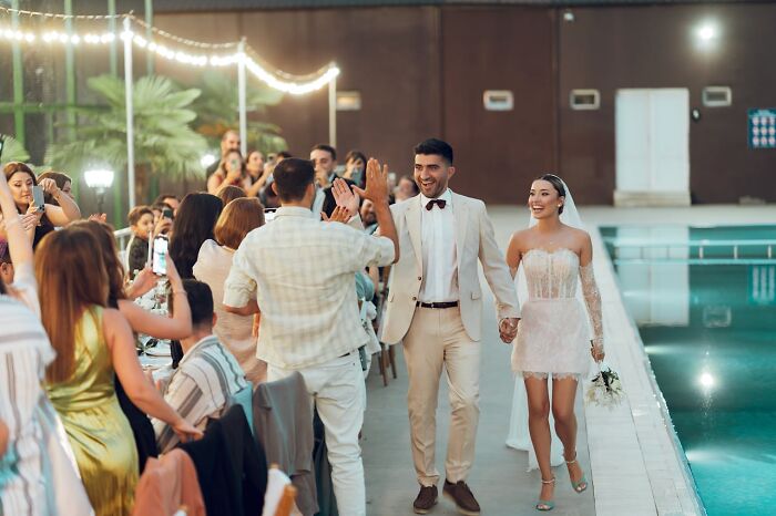 Pareja recién casada caminando junto a la piscina, celebrando con invitados en boda, sin idea del impacto accidental.