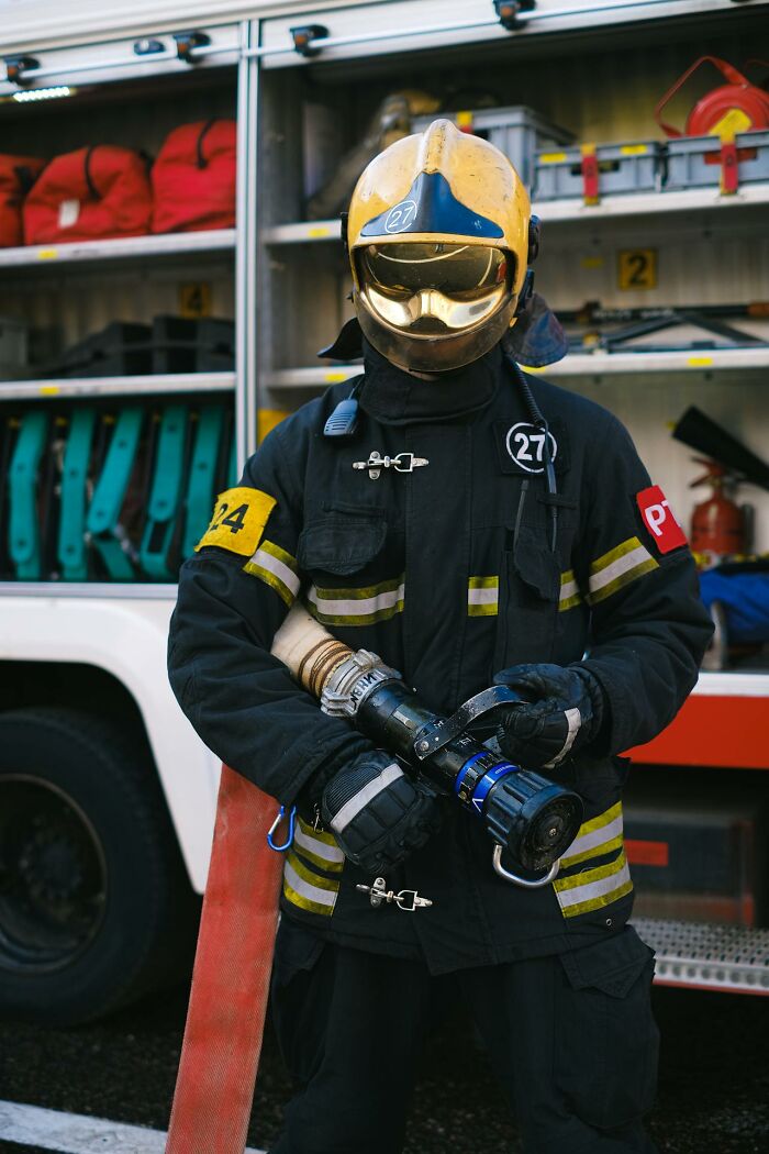 Bombero con equipo completo sosteniendo manguera frente a camión de emergencia, accidente y desastre sorprendentes.