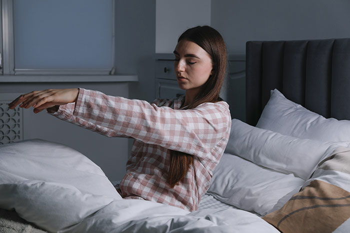 Joven sentada en cama estirando brazos en habitación oscura, inspiración para historias de Nutty Putty Cave. Joven sentada en cama estirando brazos en habitación oscura, inspiración para historias de Nutty Putty Cave.