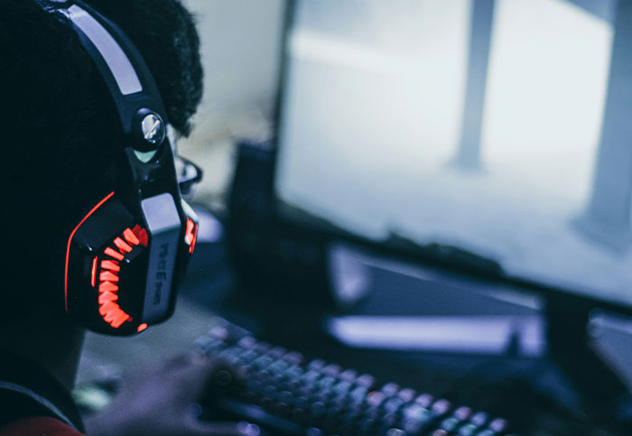 Persona con auriculares de gamer, usando computadora en escritorio oscuro, reflejando ruina y arrepentimiento personal.