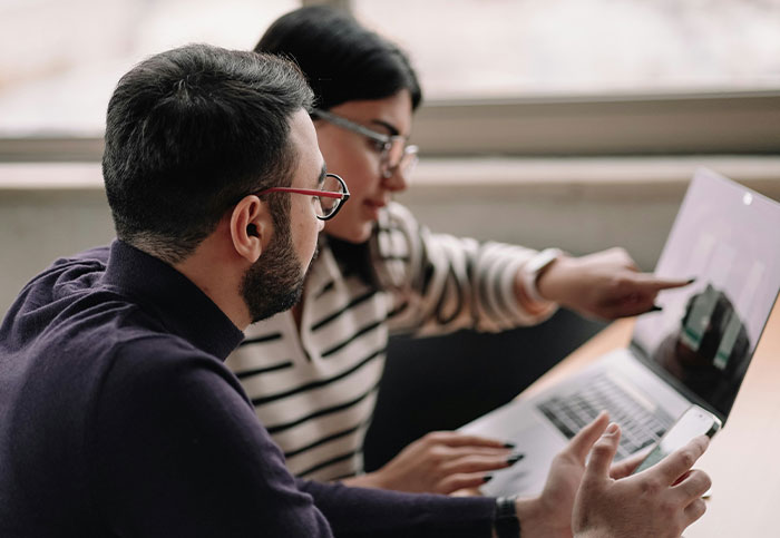 Dos personas discutiendo mientras miran y señalan la pantalla de una computadora portátil sobre confesiones y ruinar vidas.