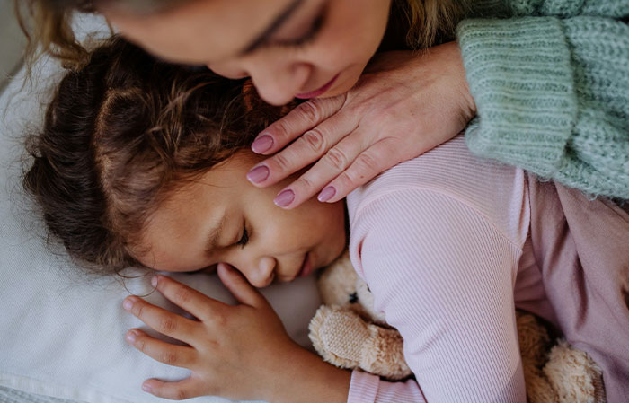 Mujer consolando a una niña dormida que abraza un peluche, reflejando sentimientos de culpa por arruinar una vida.