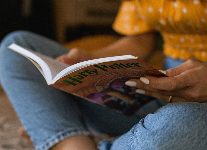 Persona sentada leyendo un libro de Harry Potter, enfoque en las manos y portada, reflexionando sobre arruinar vidas.