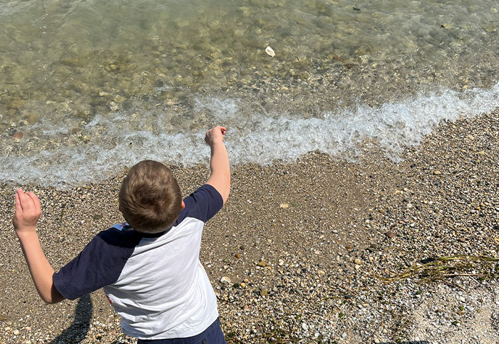 Niño lanzando piedras al agua en la orilla de una playa, simbolizando momentos de arrepentimiento y reflexión.
