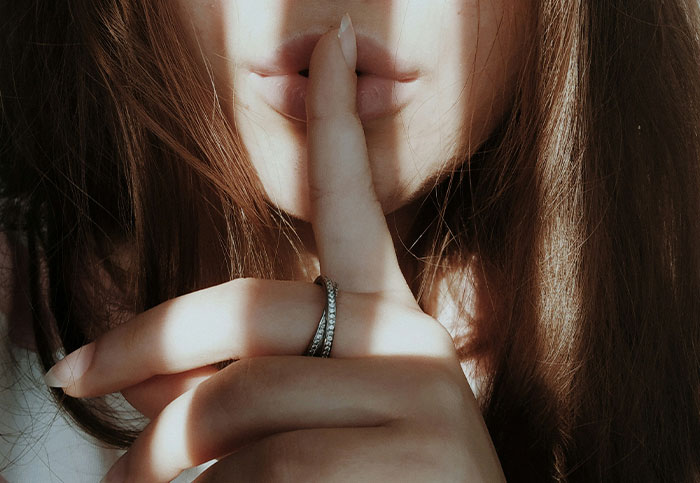 Mujer con dedo en los labios haciendo señal de silencio, representando confesiones sobre arruinar la vida de alguien.