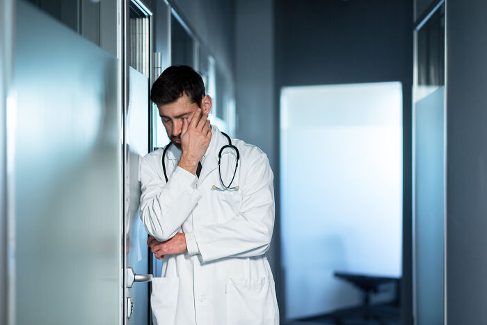 Doctor con bata blanca y estetoscopio, visiblemente angustiado en pasillo de hospital, historias de horror de médicos y enfermeras.