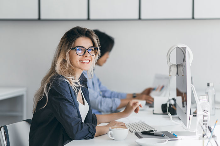 Mujer sonriente con gafas trabajando en oficina moderna mostrando consecuencias de cuando la gente miente.