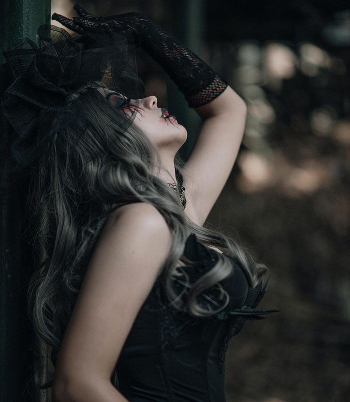 Mujer con maquillaje gótico oscuro y guantes de red posando en exterior, mostrando desconocimiento sorprendente y humorístico.
