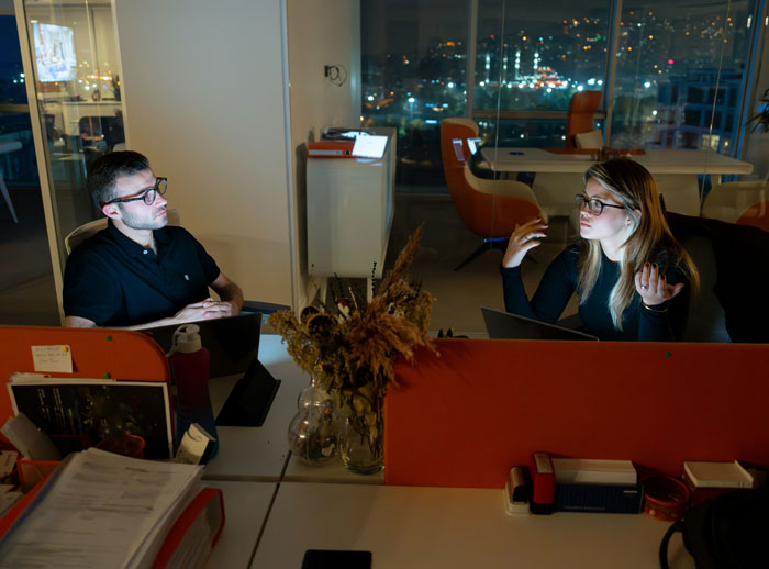 Dos personas en una oficina moderna de noche, momento inesperado y situaciones incómodas en el trabajo.