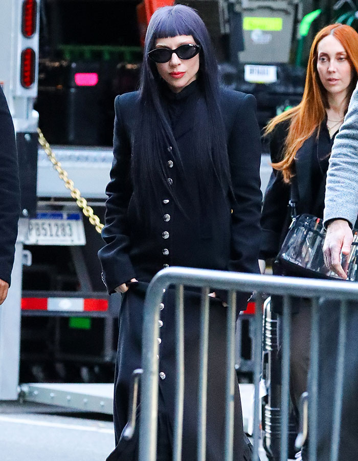 Celebridad rica con gafas de sol y vestido negro mostrando desconexión de la vida normal en la ciudad.