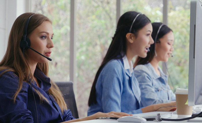 Mujeres en centro de llamadas con auriculares, imagen representando momentos inesperados y situaciones incómodas en el trabajo.