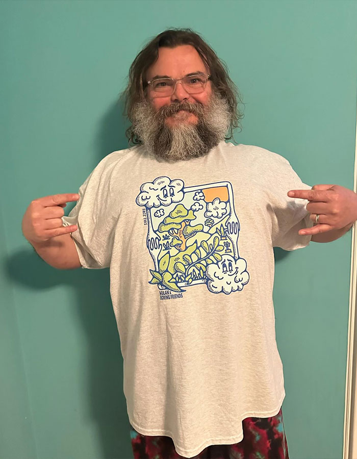 Hombre con barba y gafas mostrando una camiseta con diseño colorido relacionado con estrellas masculinas y su altura real.