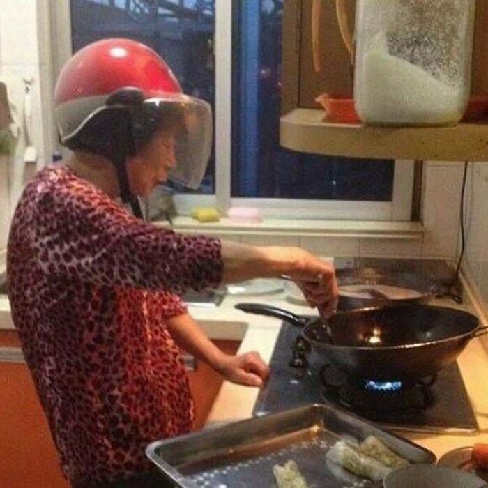 Persona mayor cocinando con un casco rojo extraño en la cocina, imagen extraña y bizarra poco común para impactar.