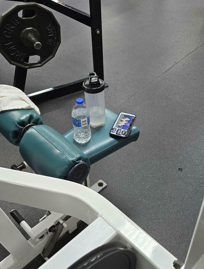 Mancuernas y botella de agua en gimnasio con teléfono mostrando video, ilustrando gente expuesta por sus acciones incorrectas.