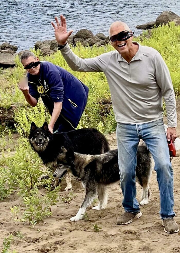 Dos hombres con perros en la playa, uno hace un gesto grosero, ejemplo de personas expuestas por su mal comportamiento.