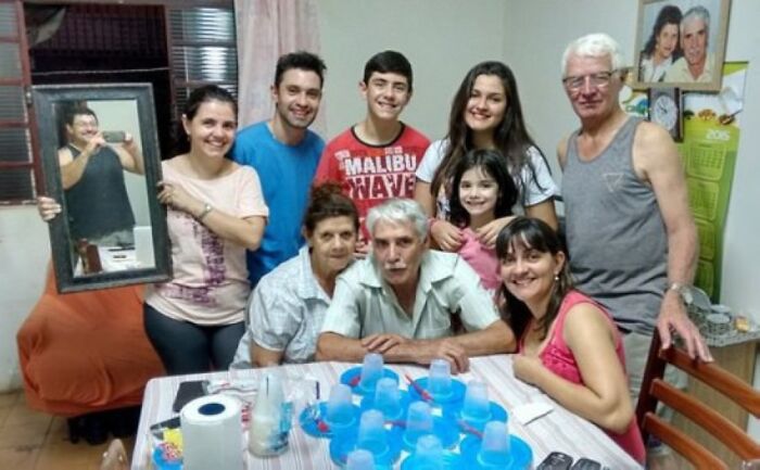 Foto familiar incómoda con varios miembros sonrientes y un espejo que refleja a la persona que toma la foto.