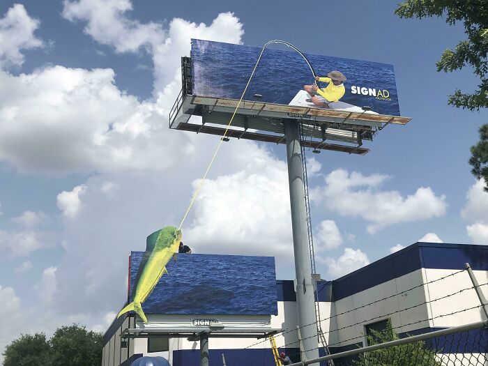 Cartel divertido y brillante con un pescador y un pez gigante que parece salido del agua, imagen curiosa para fotografiar.