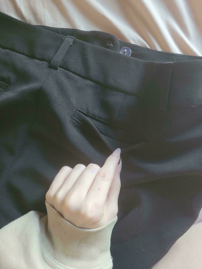 Mano intentando meter una mano en un bolsillo falso de pantalones negros, molestias leves pero muy frustrantes.