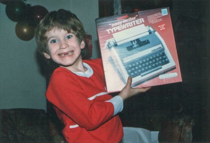 Niño sonriente sosteniendo una caja de máquina de escribir vintage, representando fotos fascinantes de los años 1980 salvajes.