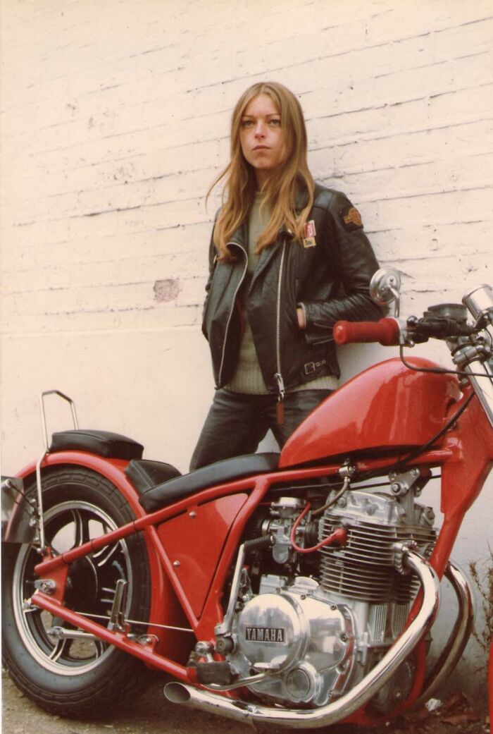 Mujer con chaqueta de cuero junto a motocicleta Yamaha roja, foto que refleja la moda y estilo de los años 1980.