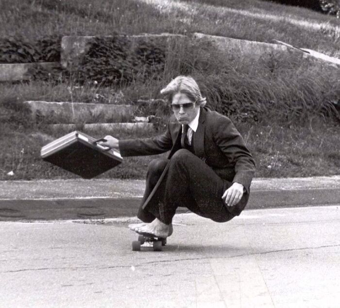 Hombre en traje con maletín en patineta, mostrando el estilo fascinante y salvaje de los años 1980.