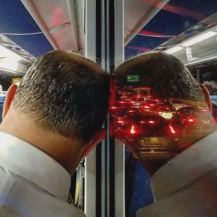 Hombre apoyando la cabeza en ventana del autobús, reflejo crea ilusión óptica con tráfico, imagen que va fuerte y causa risa.