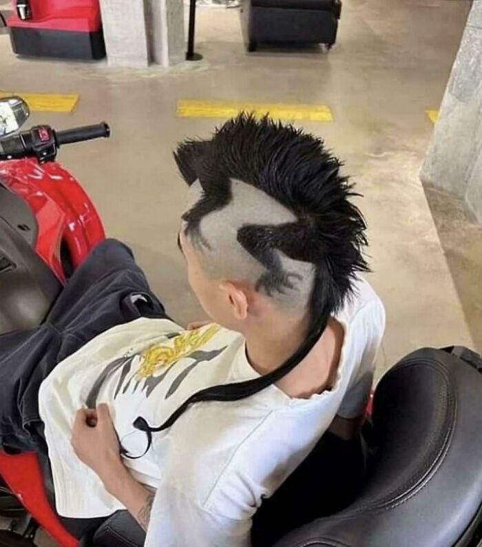 Persona con corte de cabello creativo que "va fuerte" con diseño de lagarto, sentado sobre moto roja en estacionamiento.