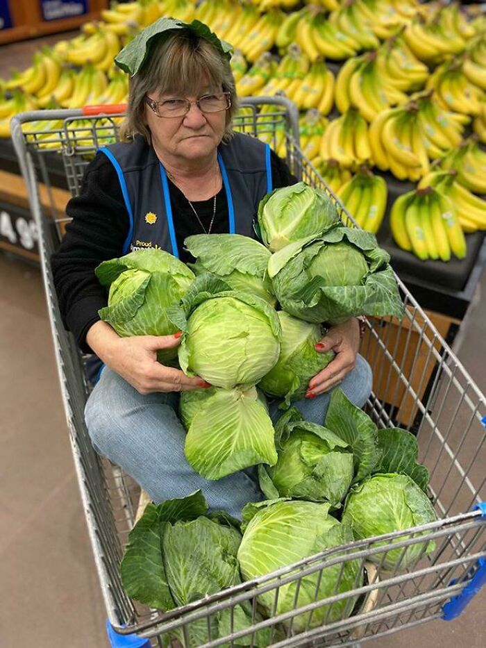Mujer en carrito de Walmart con muchas lechugas, escena divertida y confusa de People Of Walmart entre frutas y vegetales.