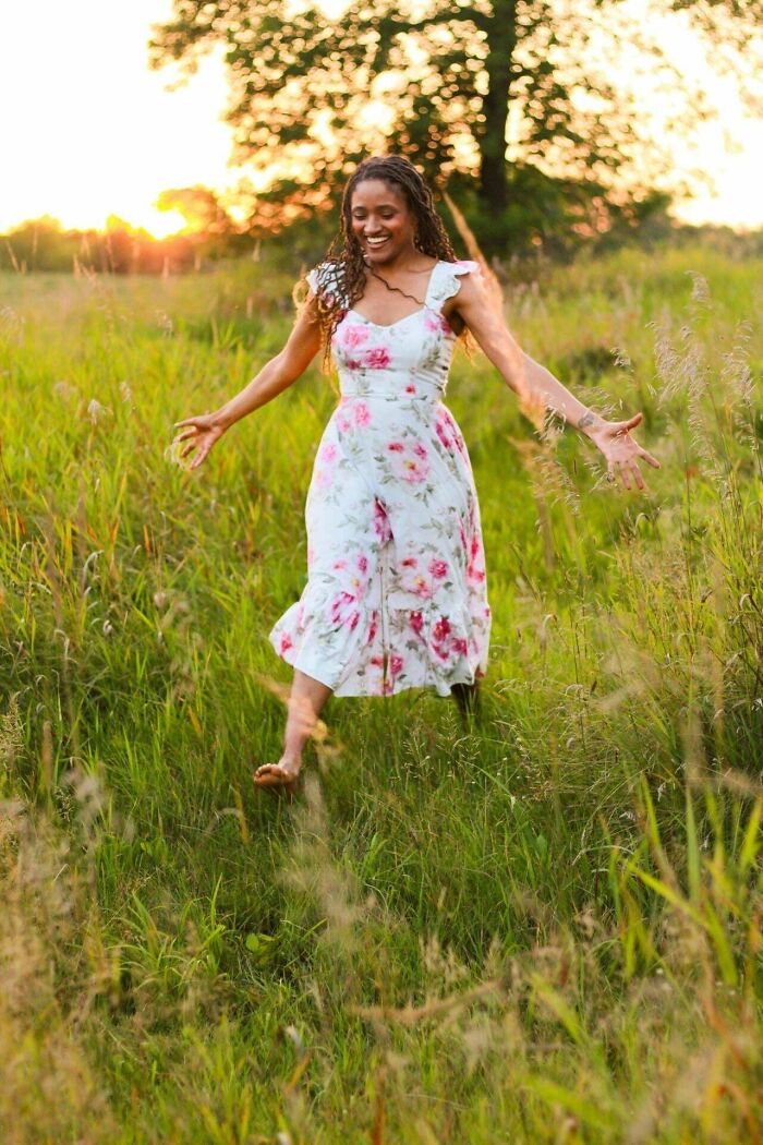 Mujer disfrutando al aire libre en un campo verde, viviendo su estilo cottagecore con vestido floral y atardecer.
