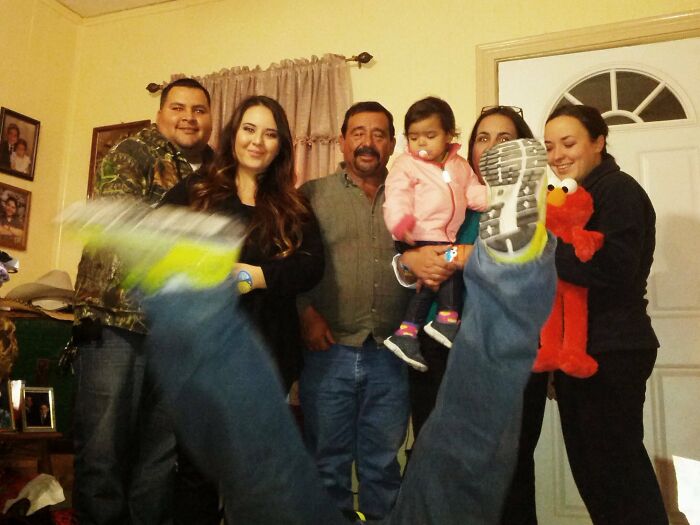 Foto familiar incómoda con miembros posando y una persona con los pies en alto, mostrando una escena familiar divertida y única.