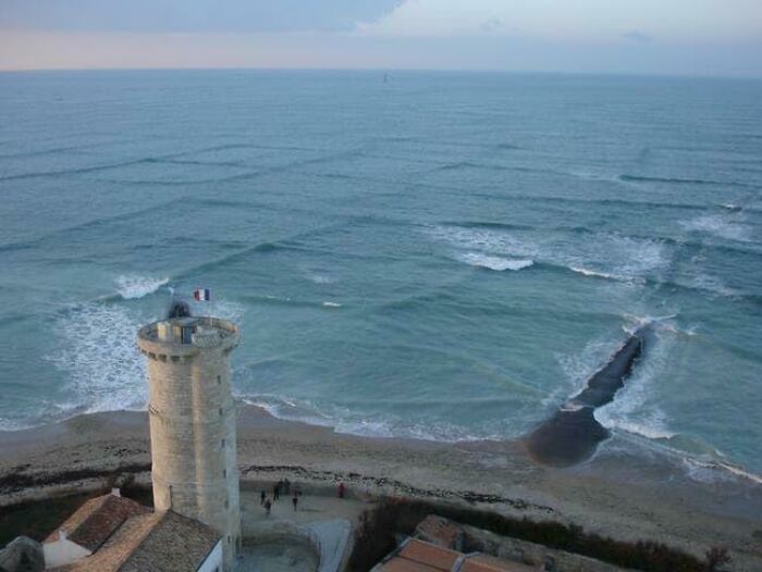 Torre antigua en la playa con patrones inusuales de olas, imagen aleatoria encontrada por personas curiosas.
