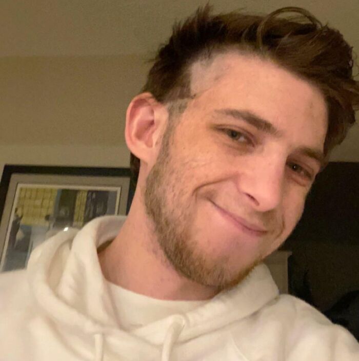 Hombre joven con una sonrisa tímida exhibiendo un accidente de cabello hilarante y trágico con corte irregular.