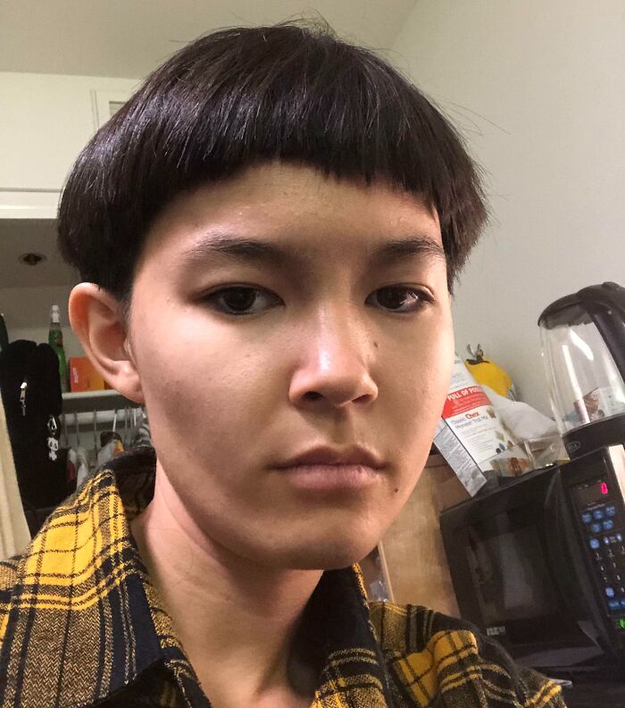 Joven con accidente de cabello hilarantemente trágico, corte de cabello irregular y expresión seria en interior.