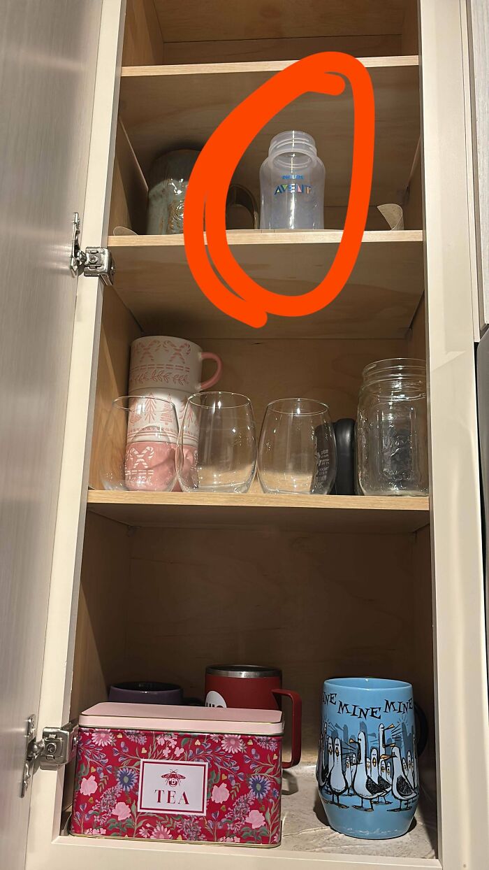 Botella misteriosa en gabinete de cocina con tazas y vasos, experiencia extraña sin explicación en un hogar común.