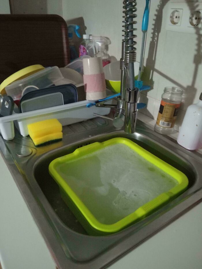 Fregadero con esponja amarilla y cubeta verde con agua, escena cotidiana de personas que experimentan cosas extrañas incomprensibles.