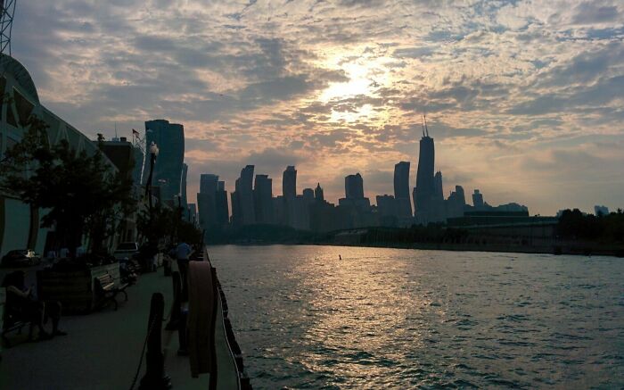 Ciudad al atardecer con rascacielos y reflejos en el río, imagen tomada como algo muy random encontrado por personas.