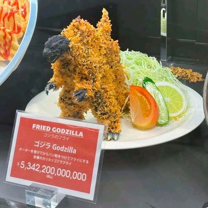 Figura de Godzilla frita con cobertura crujiente acompañada de verduras, imagen rara y bizarra.