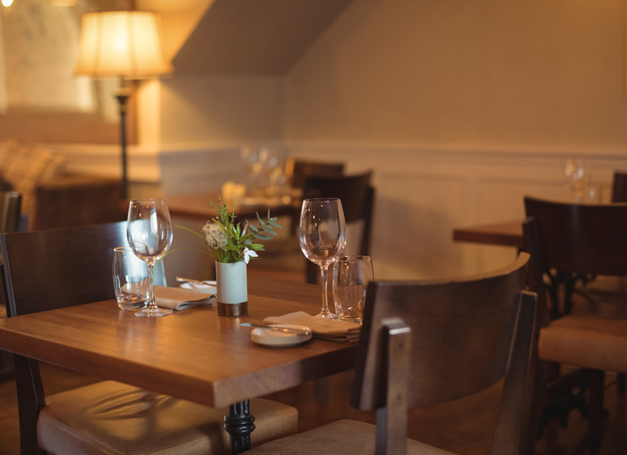Mesa de restaurante vacía con copas y decoración, representando momentos inesperados y situaciones incómodas en el trabajo.
