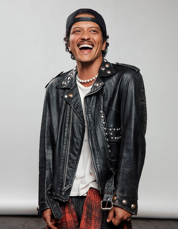 Hombre joven con chaqueta de cuero negro y gorra, sonriente y mostrando estilo moderno y actitud relajada en la fotografía.