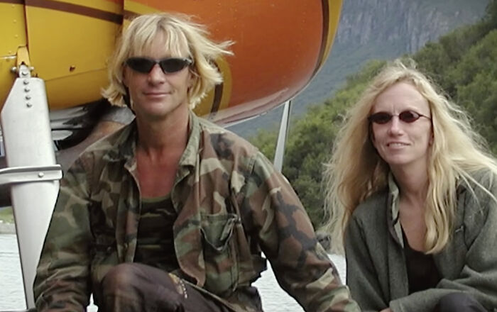 Pareja con gafas de sol frente a un helicóptero naranja, relacionado con metraje encontrado inquietante y temas de terror.