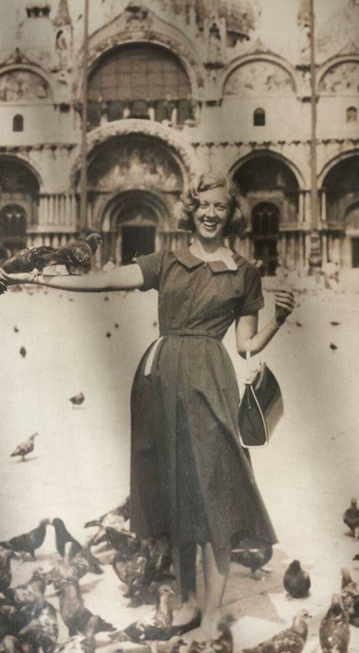 Mujer sonriente con vestido vintage y bolso, rodeada de palomas, viviendo un momento divertido en época pasada. Mujer sonriente con vestido vintage y bolso, rodeada de palomas, viviendo un momento divertido en época pasada.