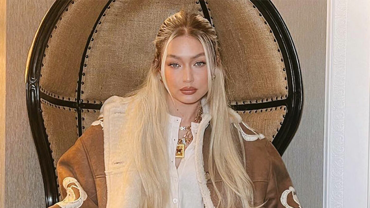 Mujer rubia en chaqueta marru00f3n sentada en silla grande, reflejando la desconexiu00f3n de ricos famosos con la vida normal.