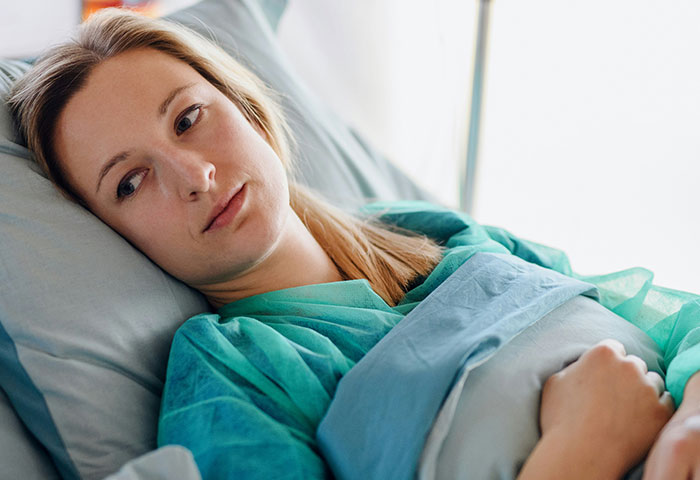 Mujer en habitación de parto con expresión pensativa representando caos tras revelarse infidelidad.