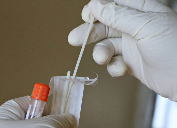 Manos con guantes manipulando hisopo y tubo de muestra, simbolizando caos en salas de parto tras descubrir infidelidad.