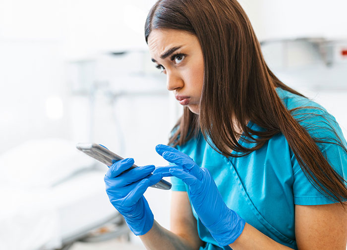 Enfermera en sala de partos revisando el teléfono con expresión preocupada tras descubrir una infidelidad y causar caos.