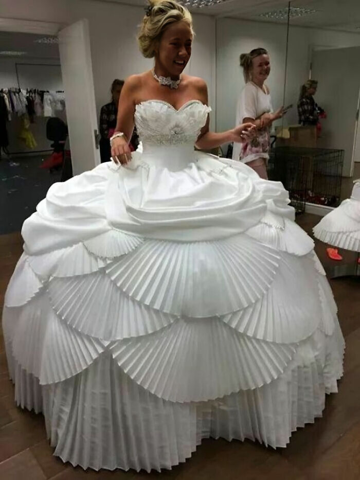 Novia sonriente con vestido de novia voluminoso y plisado en prueba dentro de una tienda de vestidos de boda.
