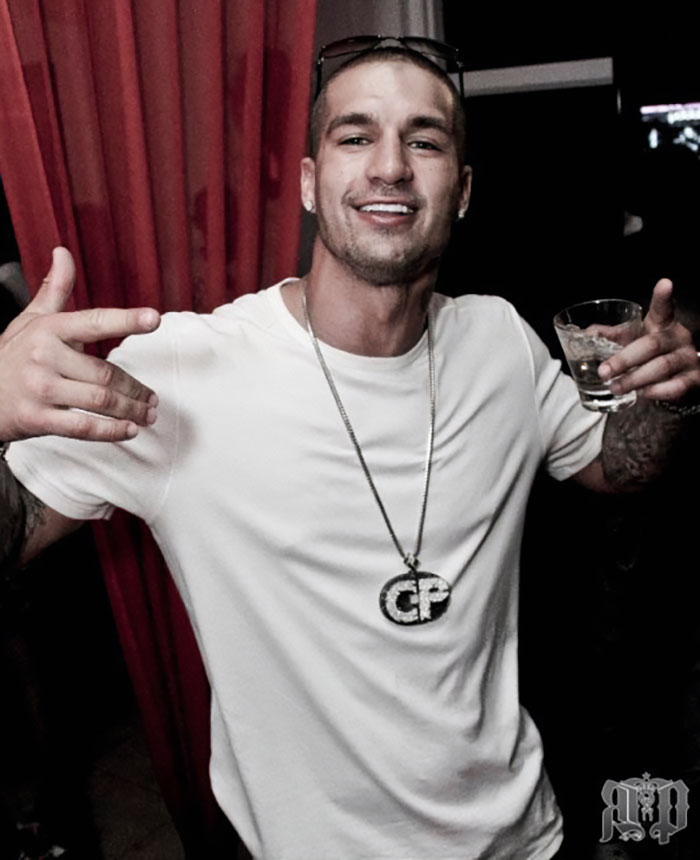 Joven sonriente con camiseta blanca y collar grande en una fiesta, relacionado con figuras públicas que desaparecieron.
