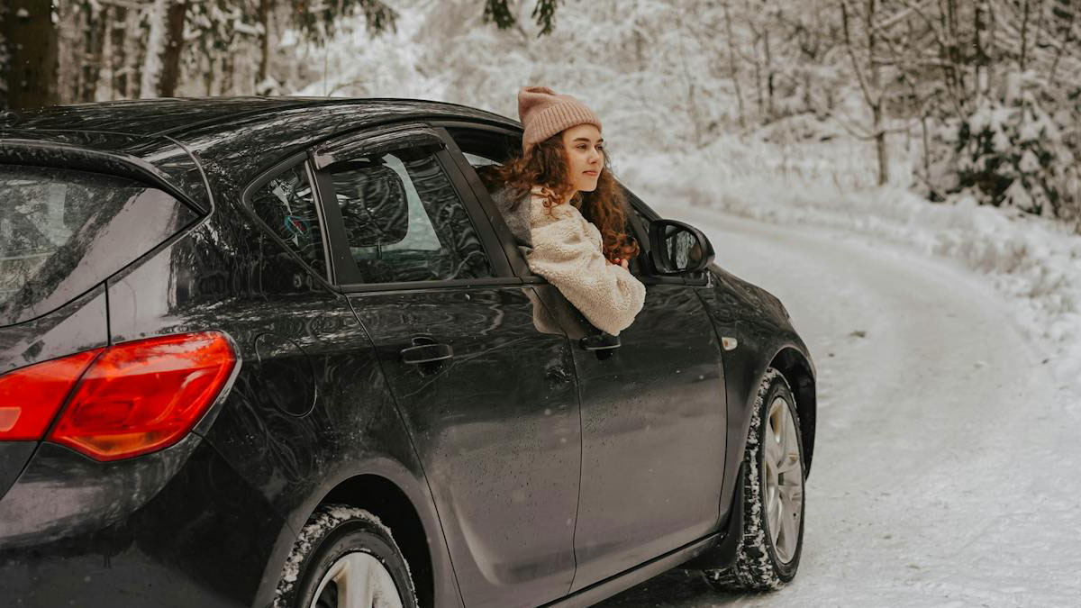 Mujer asomada por la ventana de un coche negro en un camino nevado mostrando expresiu00f3n de karma real.