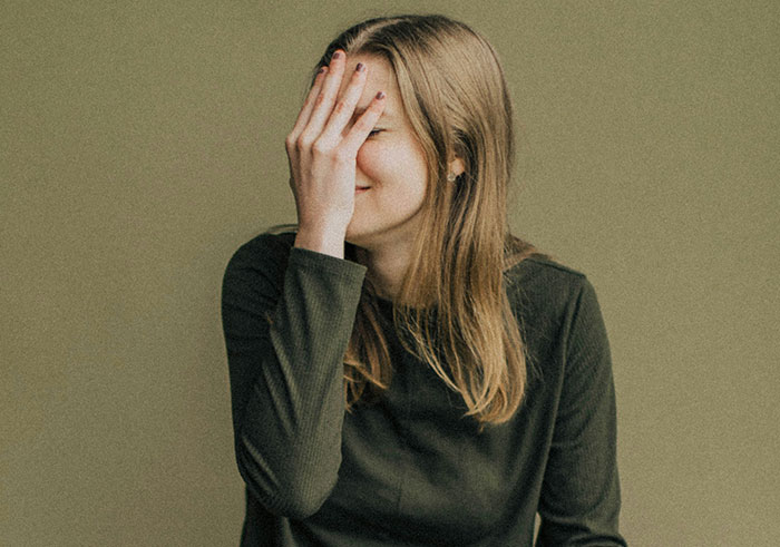 Mujer joven cubriéndose el rostro con la mano, mostrando vergüenza tras malentender señales sociales y crear cringe legendario.