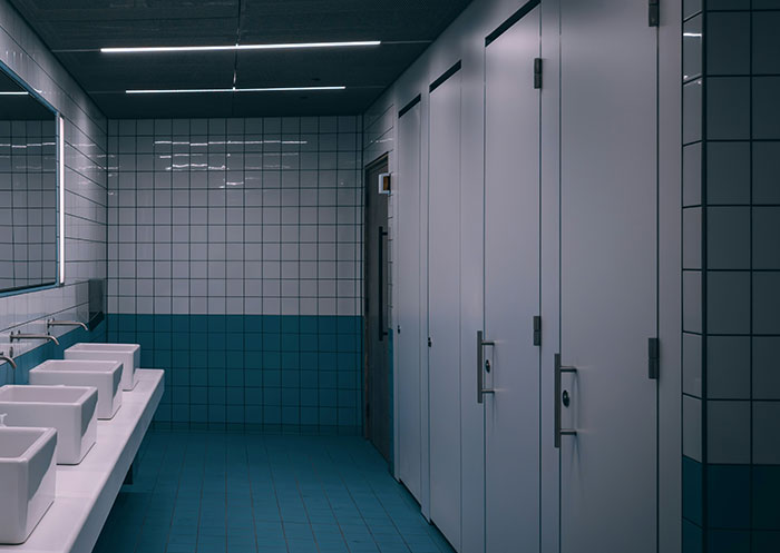 Baño público moderno con azulejos blancos y azules, reflejando incomodidad por señales sociales malinterpretadas y cringe.